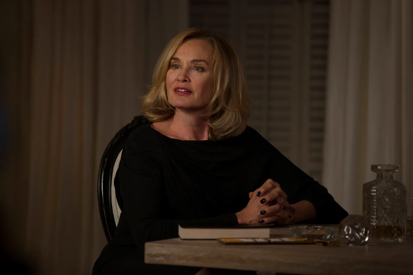 Jessica Lange as Fiona Goode sits in a black outfit inside Miss Robichaux's Academy in an official Coven publicity image.