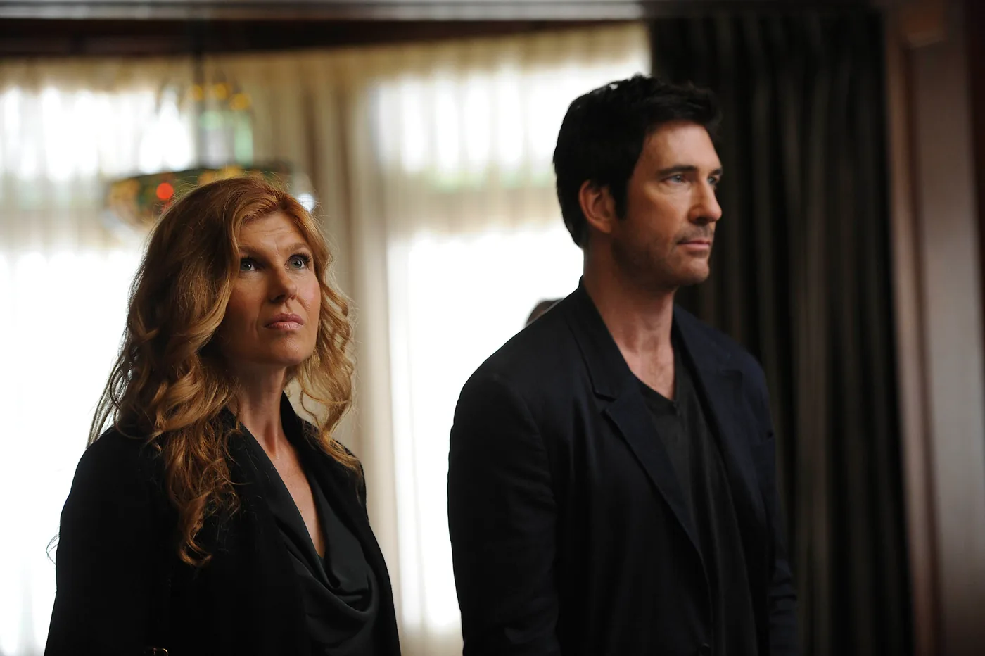 Connie Britton as Vivien Harmon stands beside Dylan McDermott as Ben Harmon in a Murder House publicity photo.