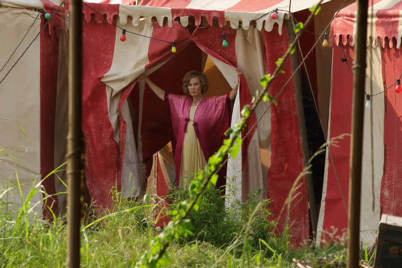 A red and cream tent stands at the center of a Freak Show publicity image, with a performer visible in its entrance.