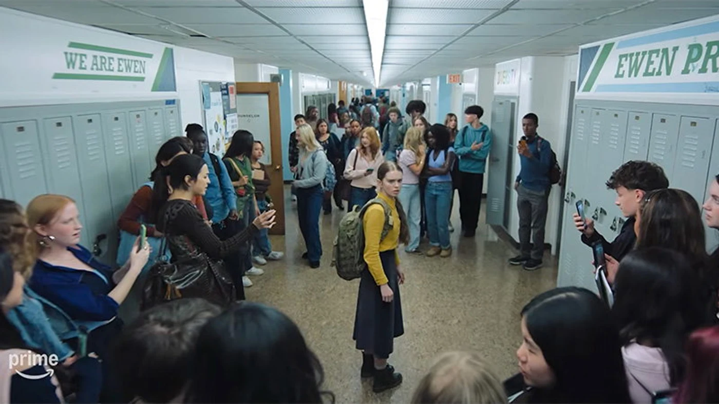 Carrie White standing alone in a crowded high-school corridor while classmates look at their phones, in the official Prime Video Carrie trailer.