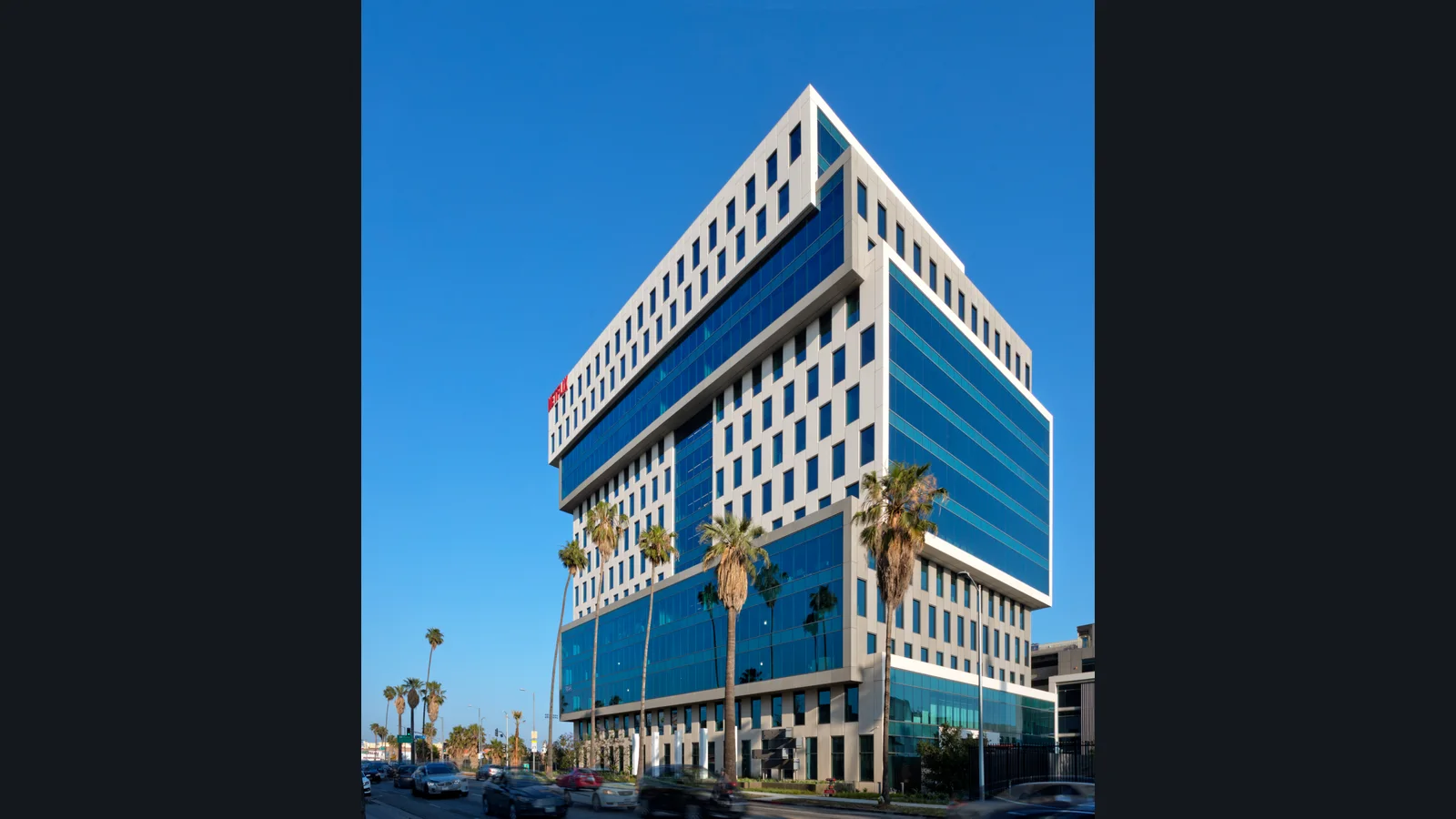 Netflix's Los Angeles office building with blue glass windows, a red Netflix sign and palm trees along the street.