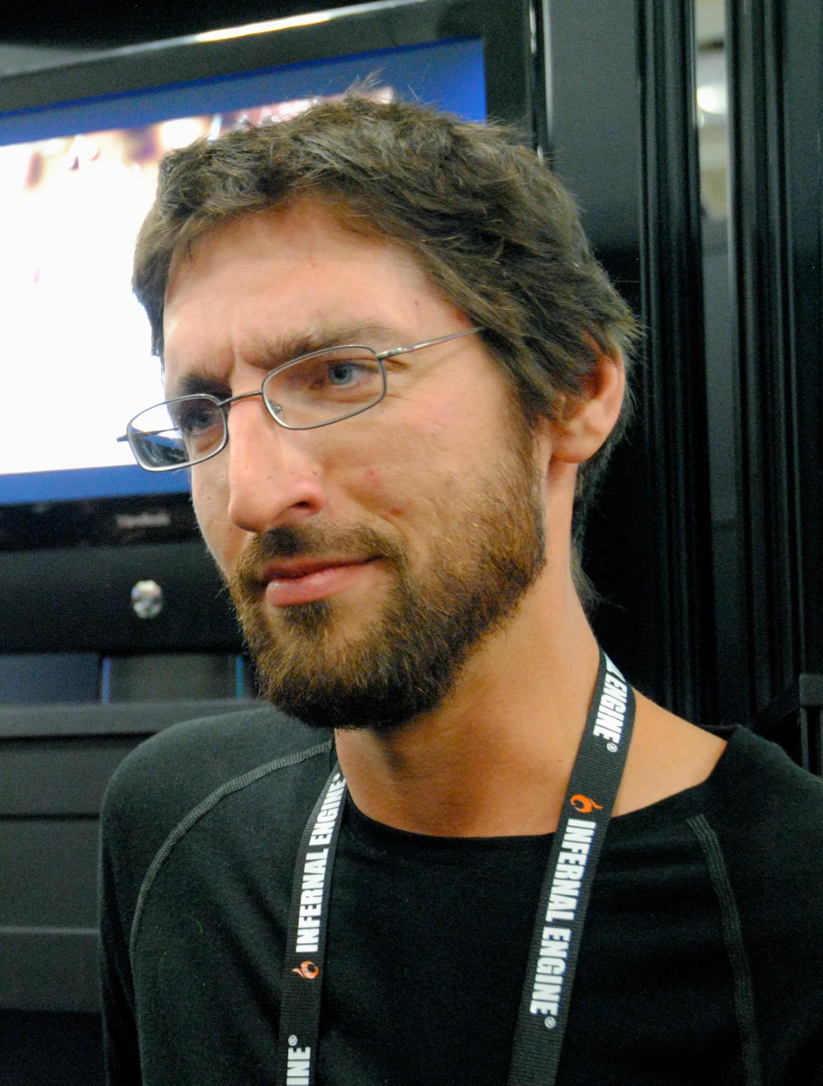 Jakub Dvorský wearing glasses and a conference lanyard in front of display screens.
