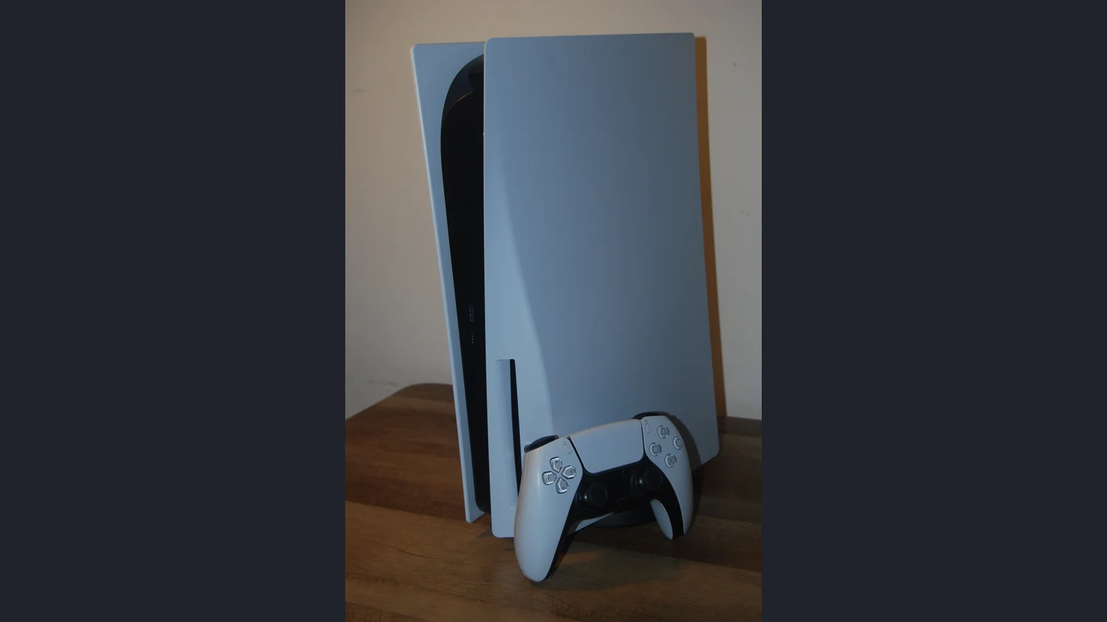 A standard PlayStation 5 console standing behind a DualSense controller.