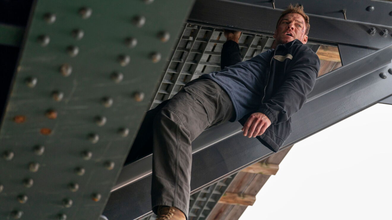 Alan Ritchson as Jack Reacher hanging beneath a steel structure in a Prime Video Season 4 promotional image.