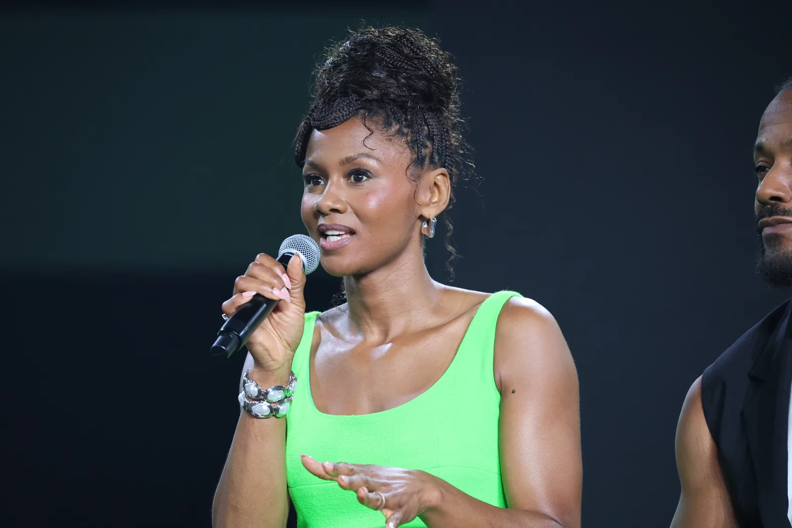Emayatzy Corinealdi in a bright green outfit speaking into a microphone at a Reasonable Doubt panel in 2025.