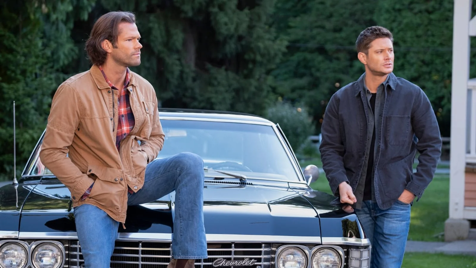 Sam and Dean Winchester, played by Jared Padalecki and Jensen Ackles, standing beside the black Chevrolet Impala in Supernatural.