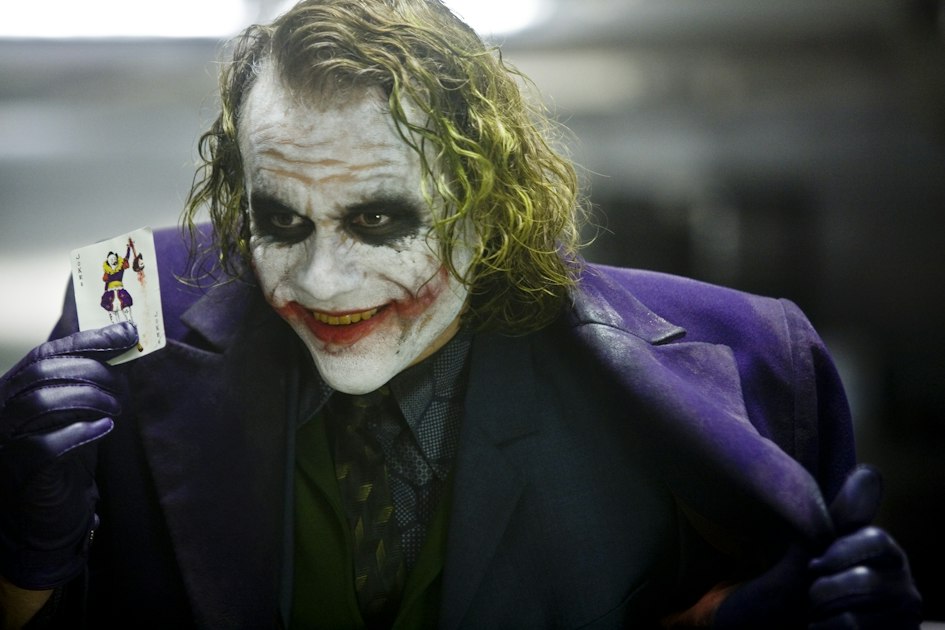Heath Ledger as the Joker holding a playing card in an official Warner Bros. still from The Dark Knight.